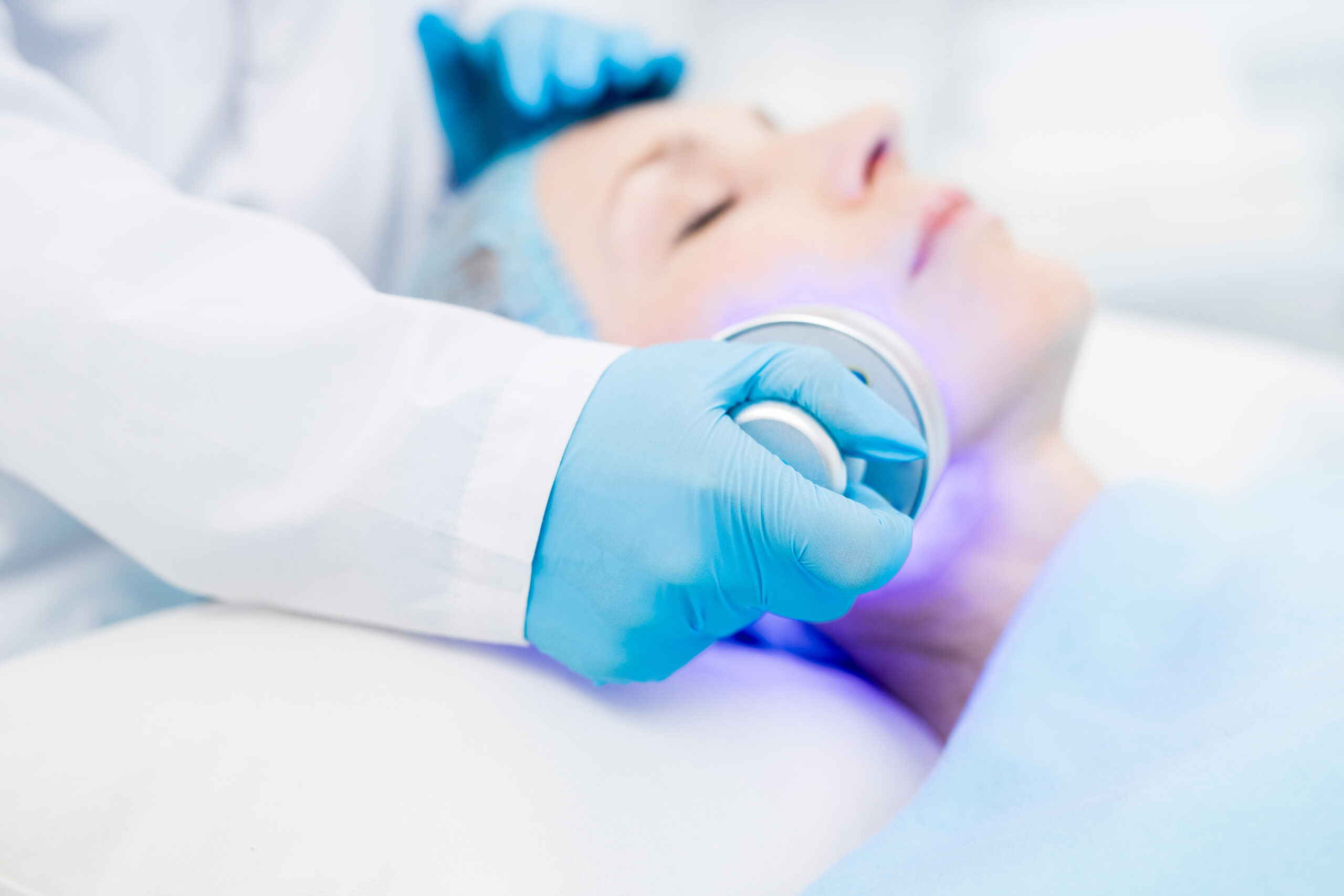 Gloved cosmetician holding electric device while making beauty procedure on client face